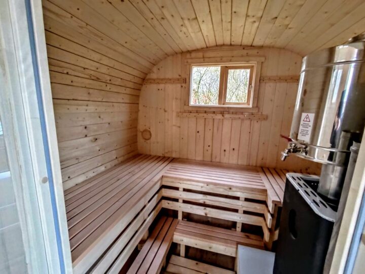 Interiör i en utomhusbastu med ljusa bänkar i trä och kamin
