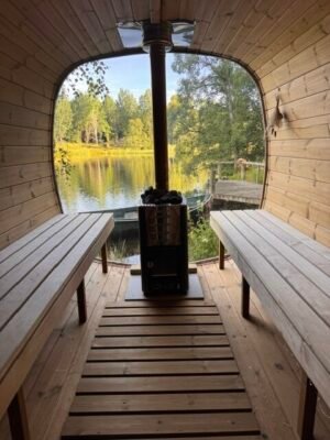 Interiör i TimberIN Nordic Square mobilbastu med träbänkar och vedeldad kamin vid en sjö