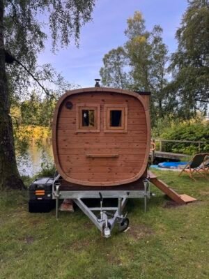 Framifrån: TimberIN Nordic Square mobilbastu på släp vid en sjö