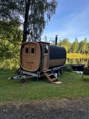 Från sidan: TimberIN Nordic Square mobilbastu på släp med skorsten vid en sjö