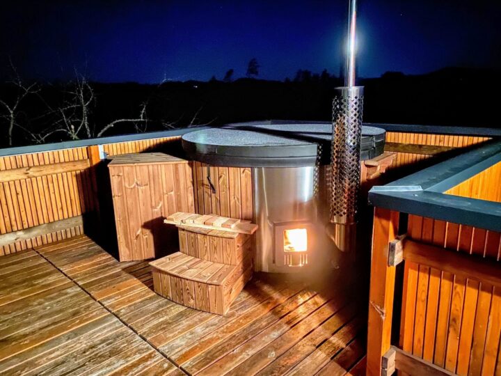 Badtunna med tänd vedkamin och skorsten på en terrass en kväll